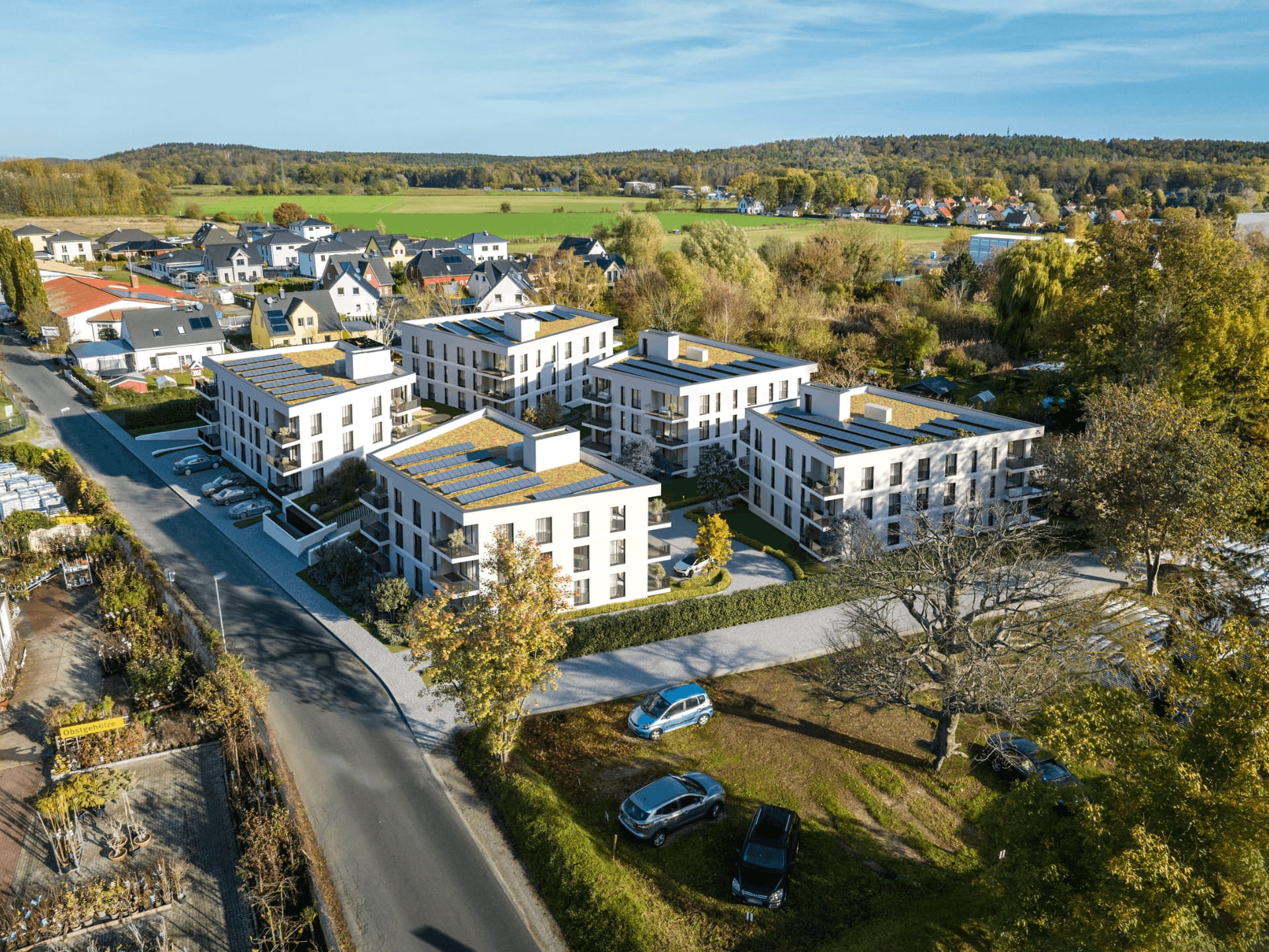 Fotorealistische 3D-Architekturvisualisierung eines modernen Neubauquartiers aus der Vogelperspektive. Die detaillierte Luftaufnahme zeigt ein geplantes Wohnprojekt mit mehreren weißen Mehrfamilienhäusern, die mit nachhaltigen Gründächern und Photovoltaikanlagen ausgestattet sind. Moderne Balkone, großzügige Fensterfronten und ansprechende Außenanlagen mit Parkplätzen runden das Architekturkonzept ab. Die Gebäude fügen sich harmonisch in die umliegende grüne Vorstadtlandschaft ein – ein ideales Bild für die professionelle Immobilienvermarktung und Projektentwicklung.
